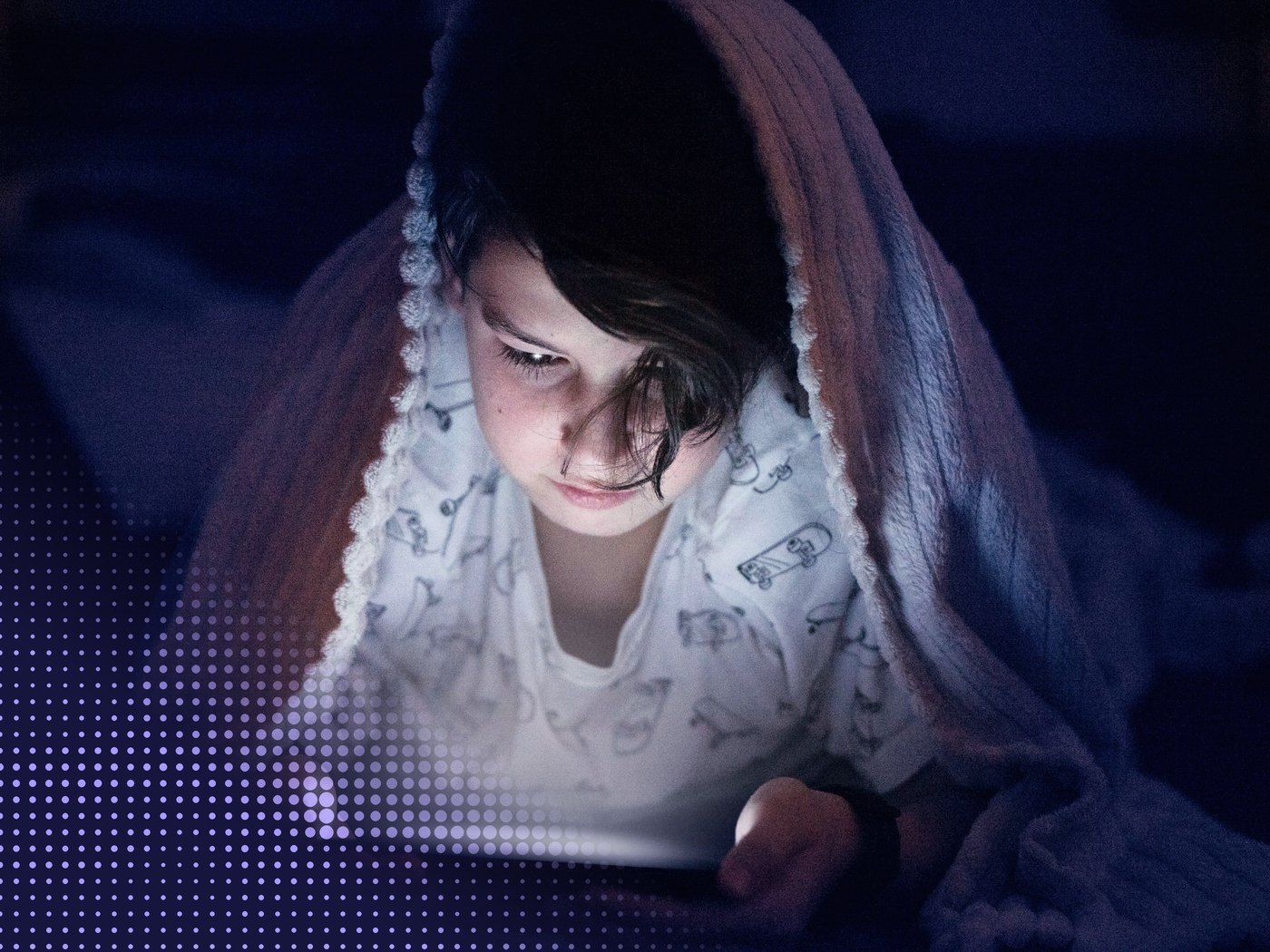 Niña bajo una frazada mirando una pantalla de noche