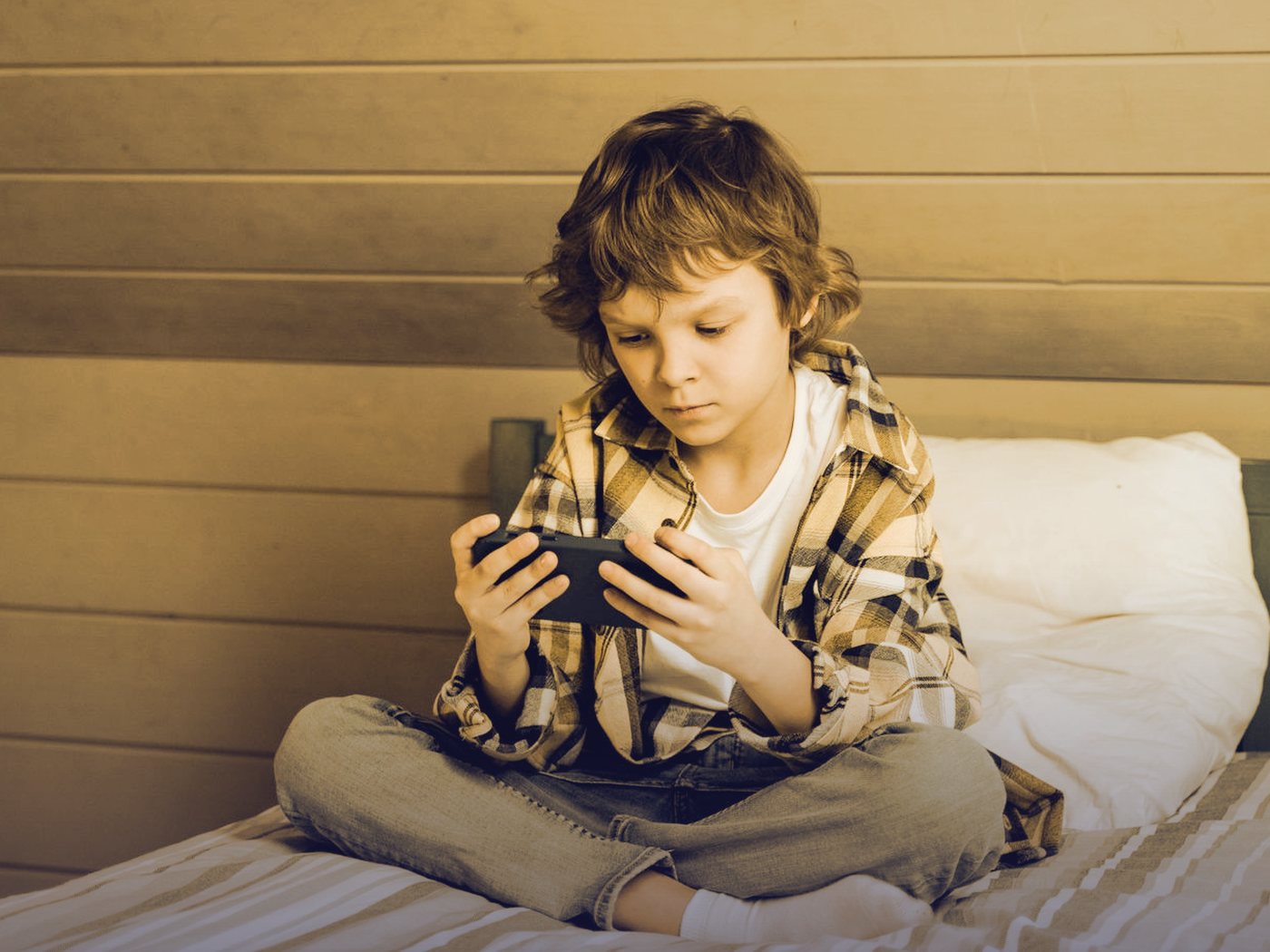 Niño concentrado jugando con el celular en su cama