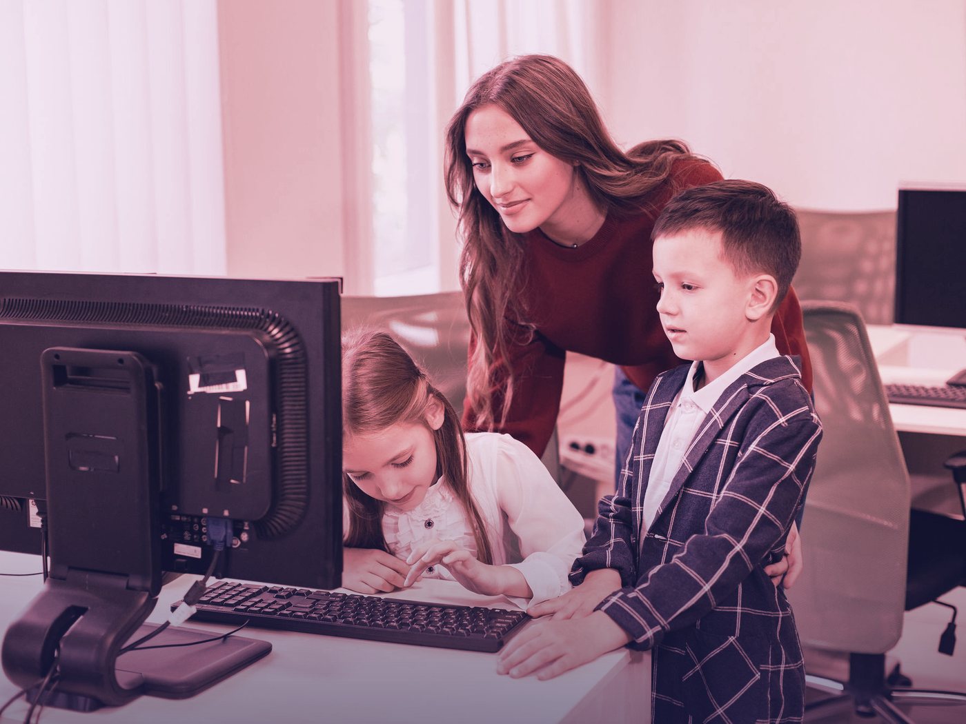 Docente ayudando a dos estudiantes en el computador