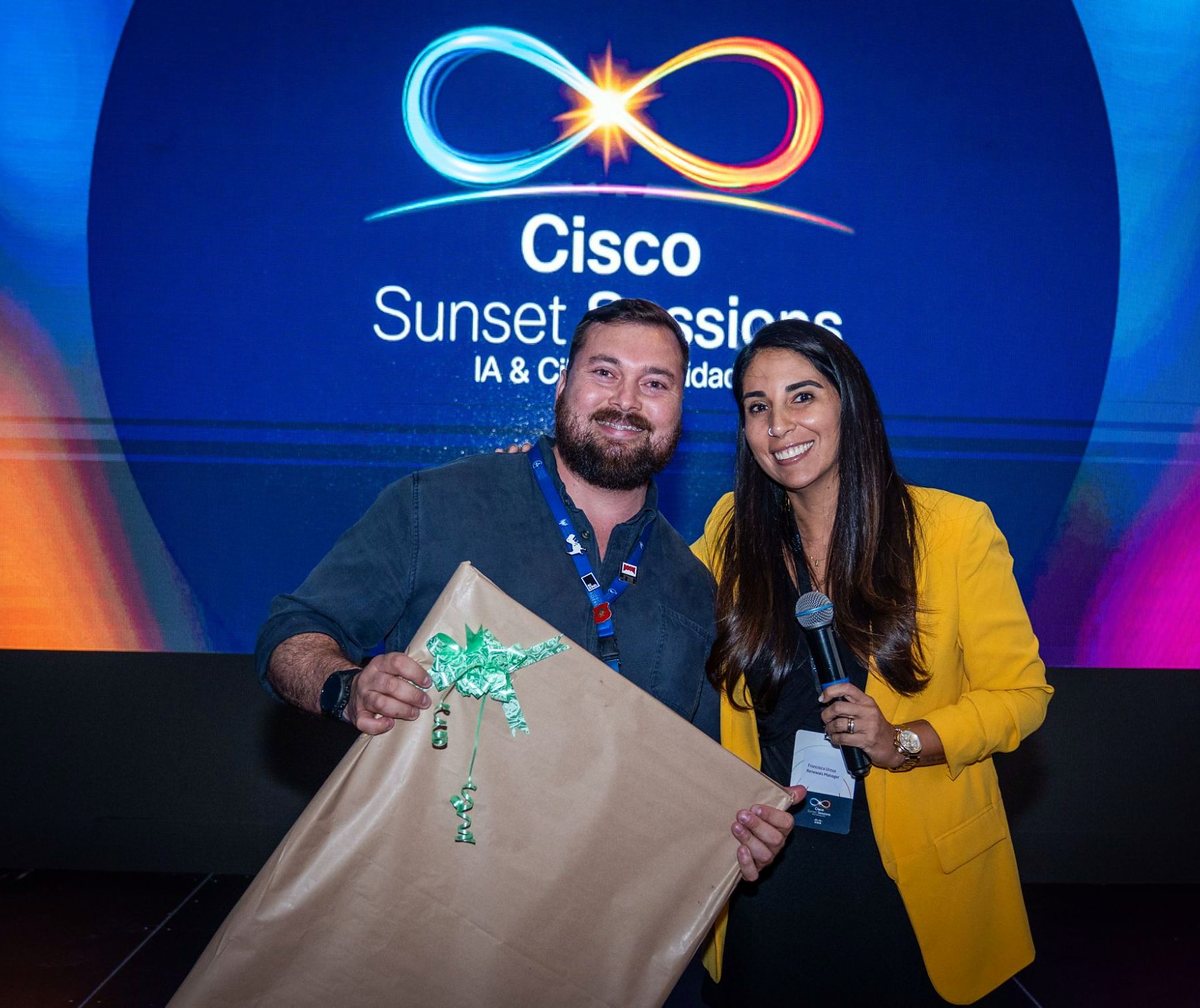 Hugo Miranda sonríe con su premio, un regalo envuelto en papel kraft, junto a la animadora del evento frente a la pantalla de Cisco Sunset Sessions.