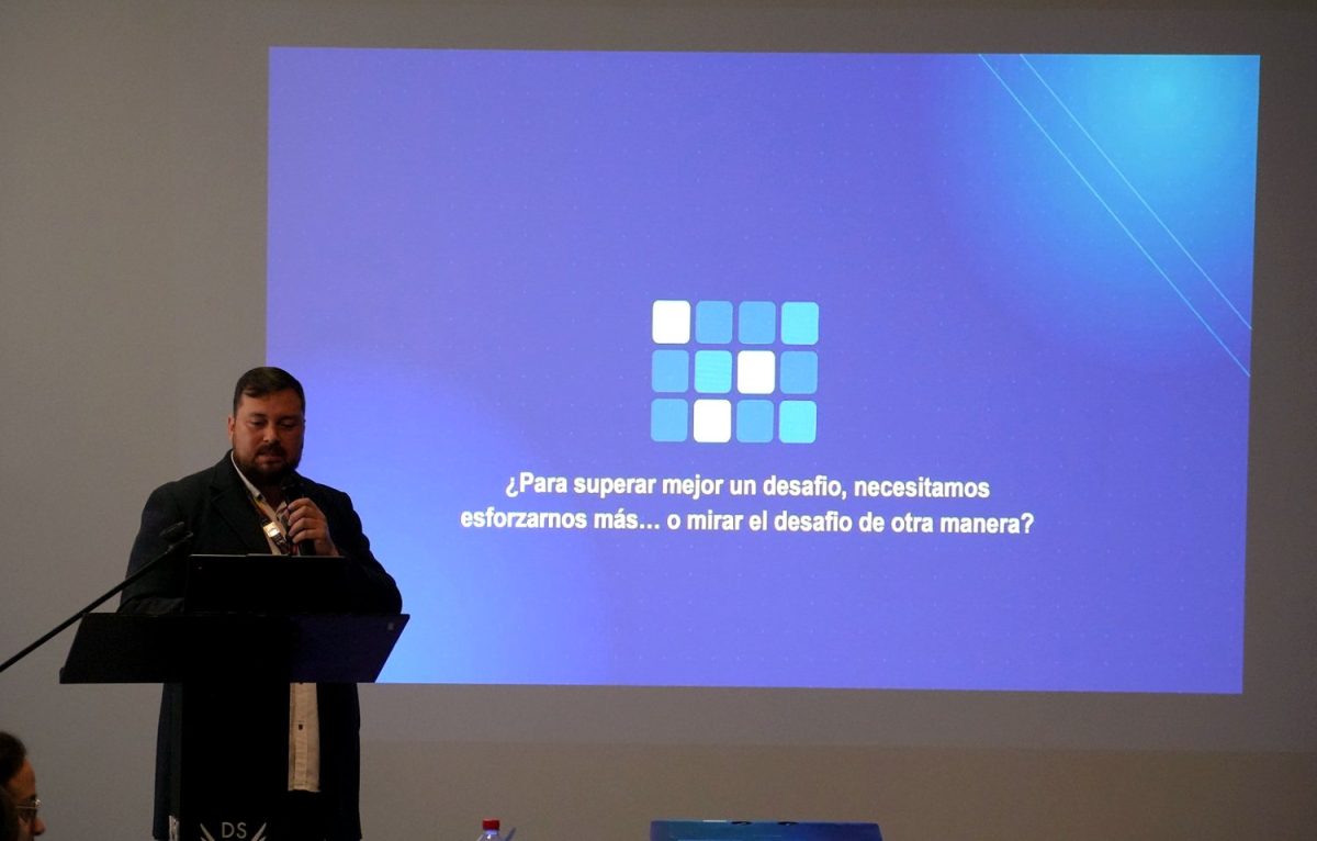 Hugo Miranda habla desde el atril junto a una lámina azul que pregunta: «¿Para superar mejor un desafío, necesitamos esforzarnos más… o mirar el desafío de otra manera?».