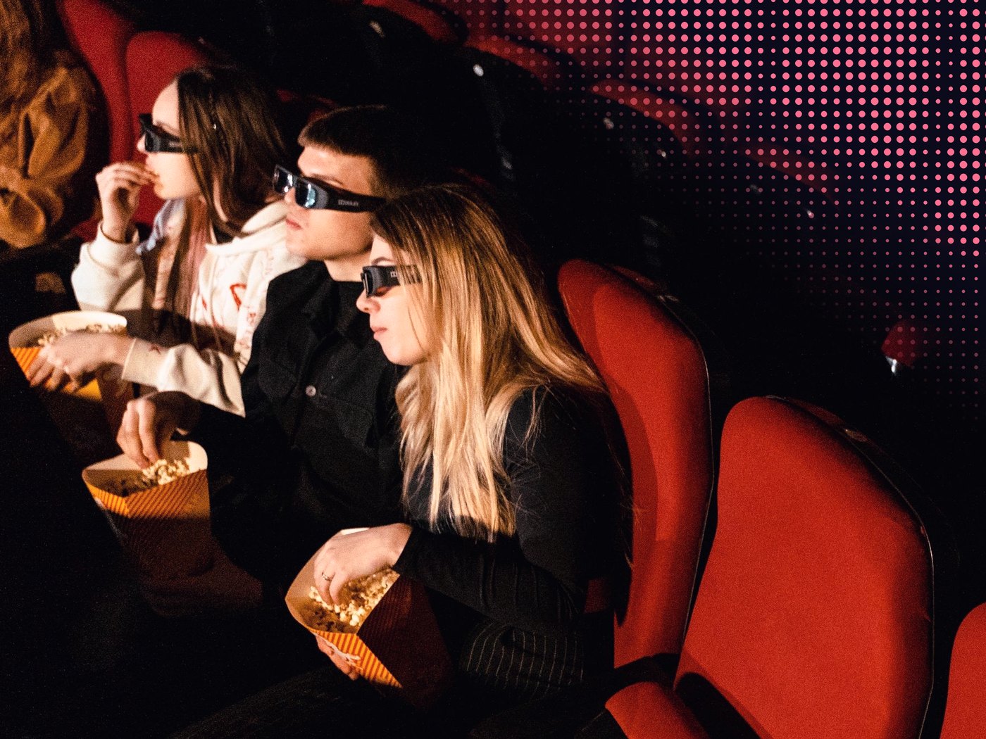 Tres amigos con lentes 3D comiendo cabritas en una sala de cine