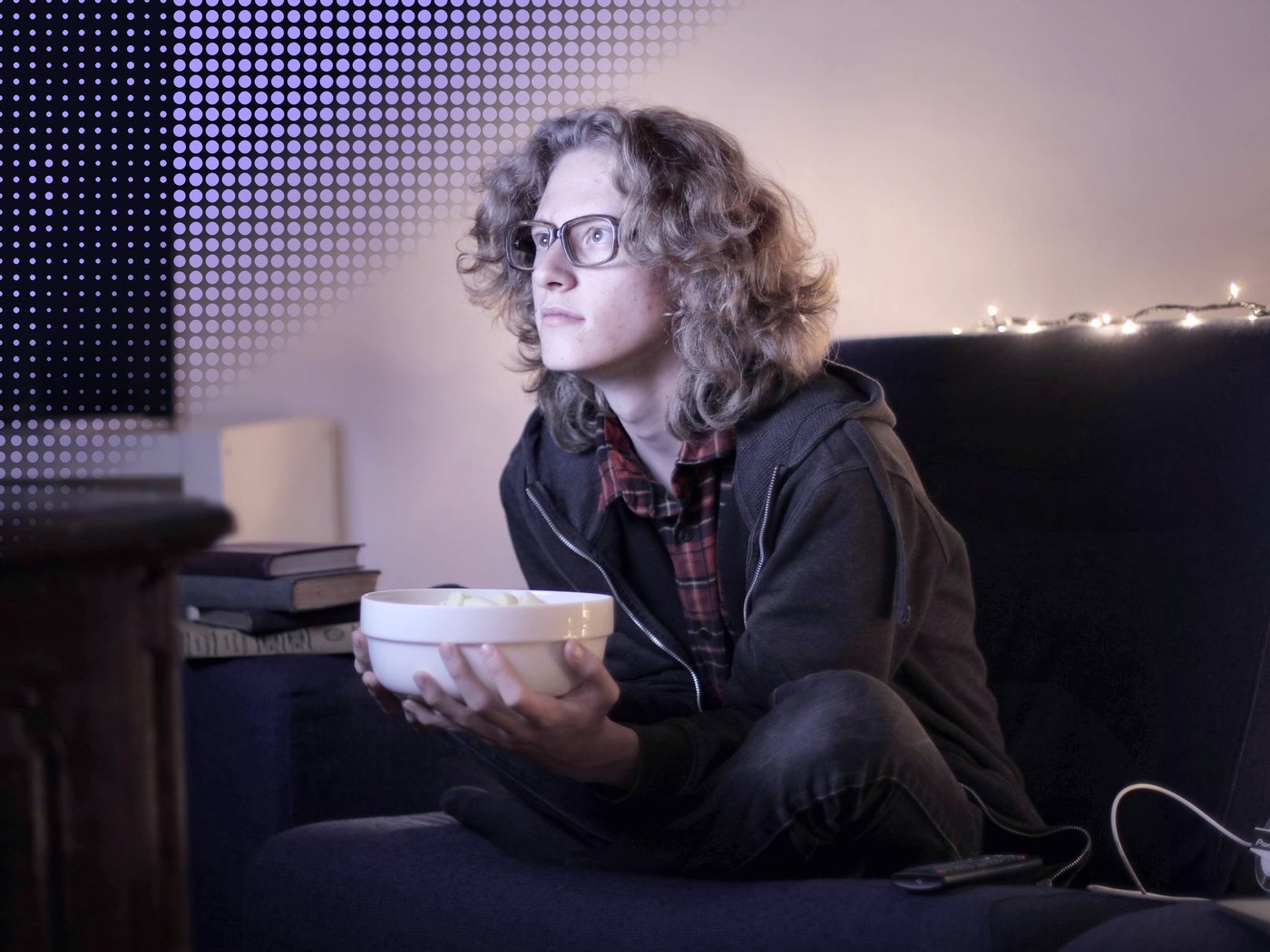 Joven con lentes y un bol de cabritas mirando una pantalla de noche