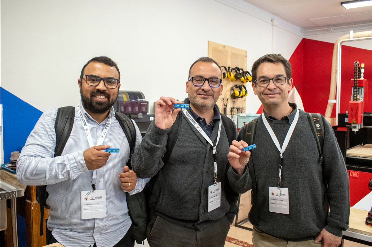 Tres participantes de la Informatik Konferenz 2026 sonríen en el FabLab mostrando llaveros con las teclas Ctrl, Alt y Del.