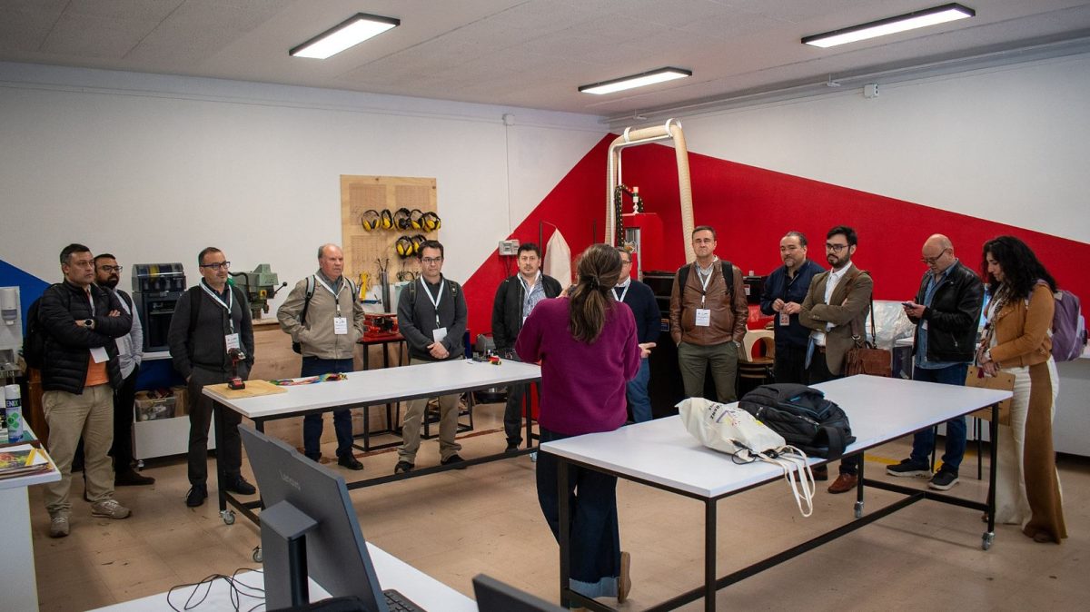 Participantes de la Informatik Konferenz 2026 escuchan una explicación en el FabLab del Deutsche Schule de Viña del Mar, entre mesas de trabajo, una impresora 3D y una fresadora CNC.