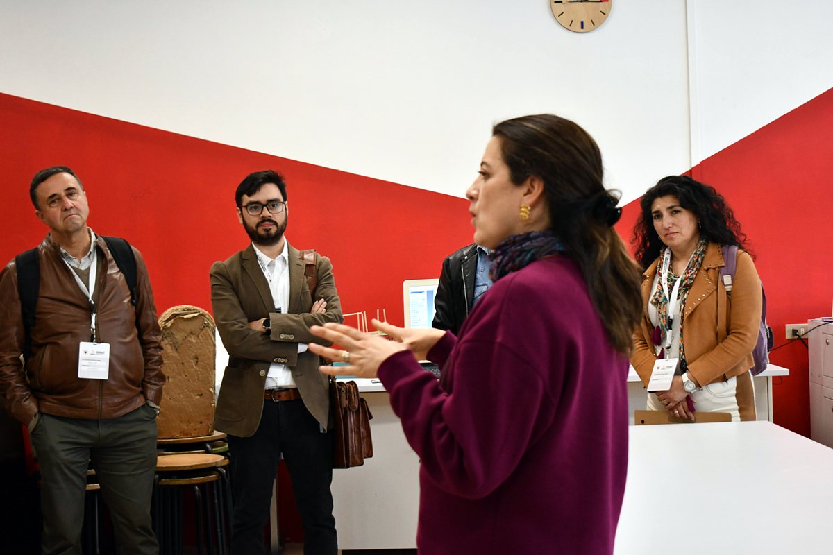 Una expositora explica el trabajo del FabLab a participantes de la Informatik Konferenz 2026, frente a una pared roja.